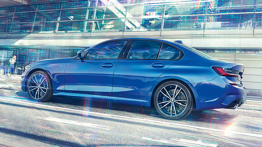 BMW 3 Series Sedan (G20) during the day in front of building made of glass. Static side view of the BMW 3 Series Sedan (G20) Portimao Blue during day in front of building made of glass.
