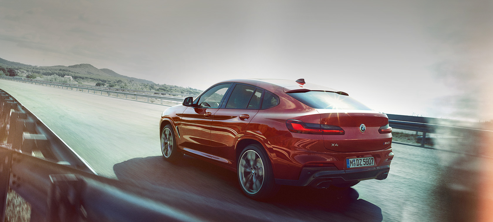 BMW X4 M40i G02 2018 Flamenco Red brilliant effect three-quarter rear view driving on the road