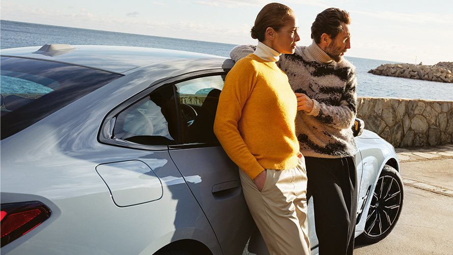 BMW Service Inclusive duration and contractual periods for new cars BMW Service Inclusive man and woman lean on BMW i4 in front of coast