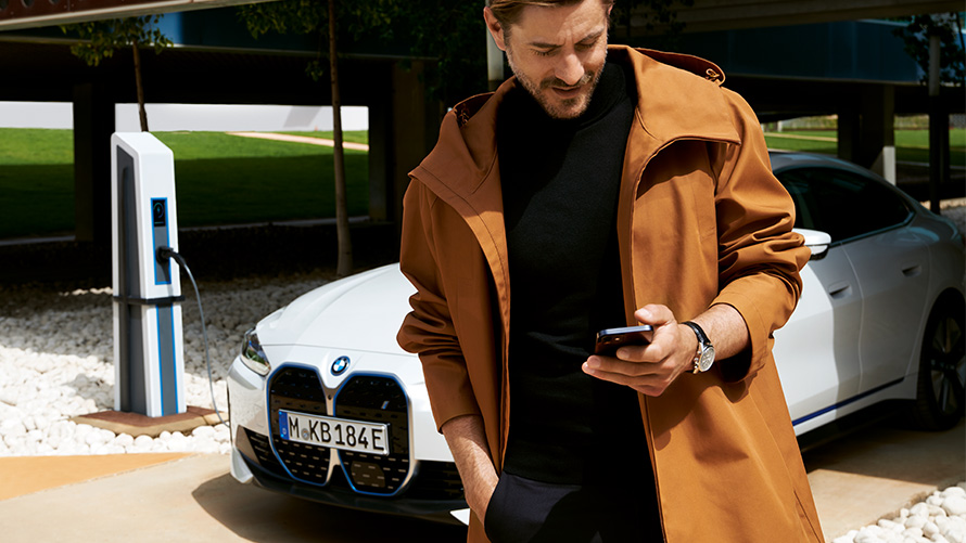 BMW Service Inclusive duration and contractual periods for electric vehicles BMW Service Inclusive man looks at smartphone in front of BMW i4 at charging station